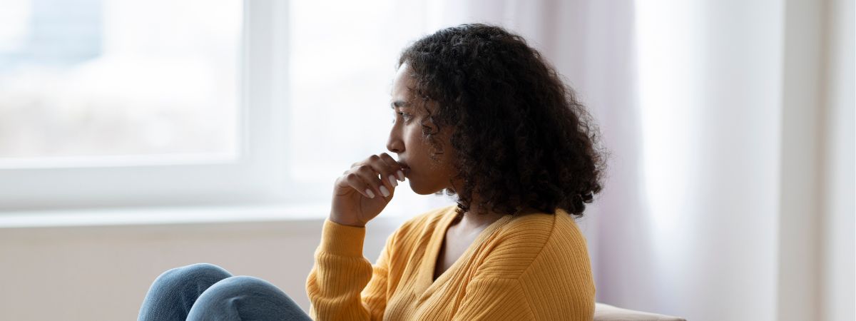 A sad woman looking out the window sitting on a couch